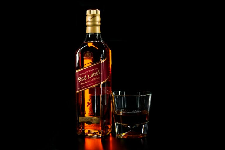 Close-up of a whiskey bottle and glass on a dark background, highlighting the amber color and glossy reflection.